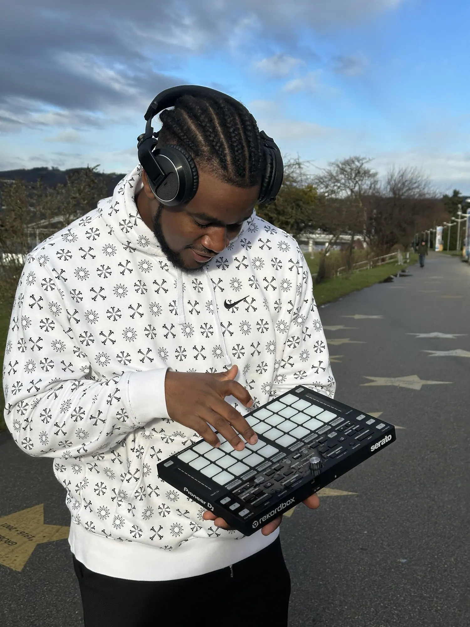 DJ Pharoh in headphones under a wide blue sky, playing a pad controller held in one hand.