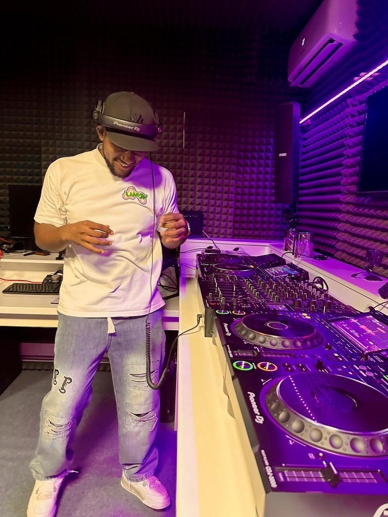 DJ Pharoh mixing at the decks in Pioneer DJ headphones, grinning down at the controller.